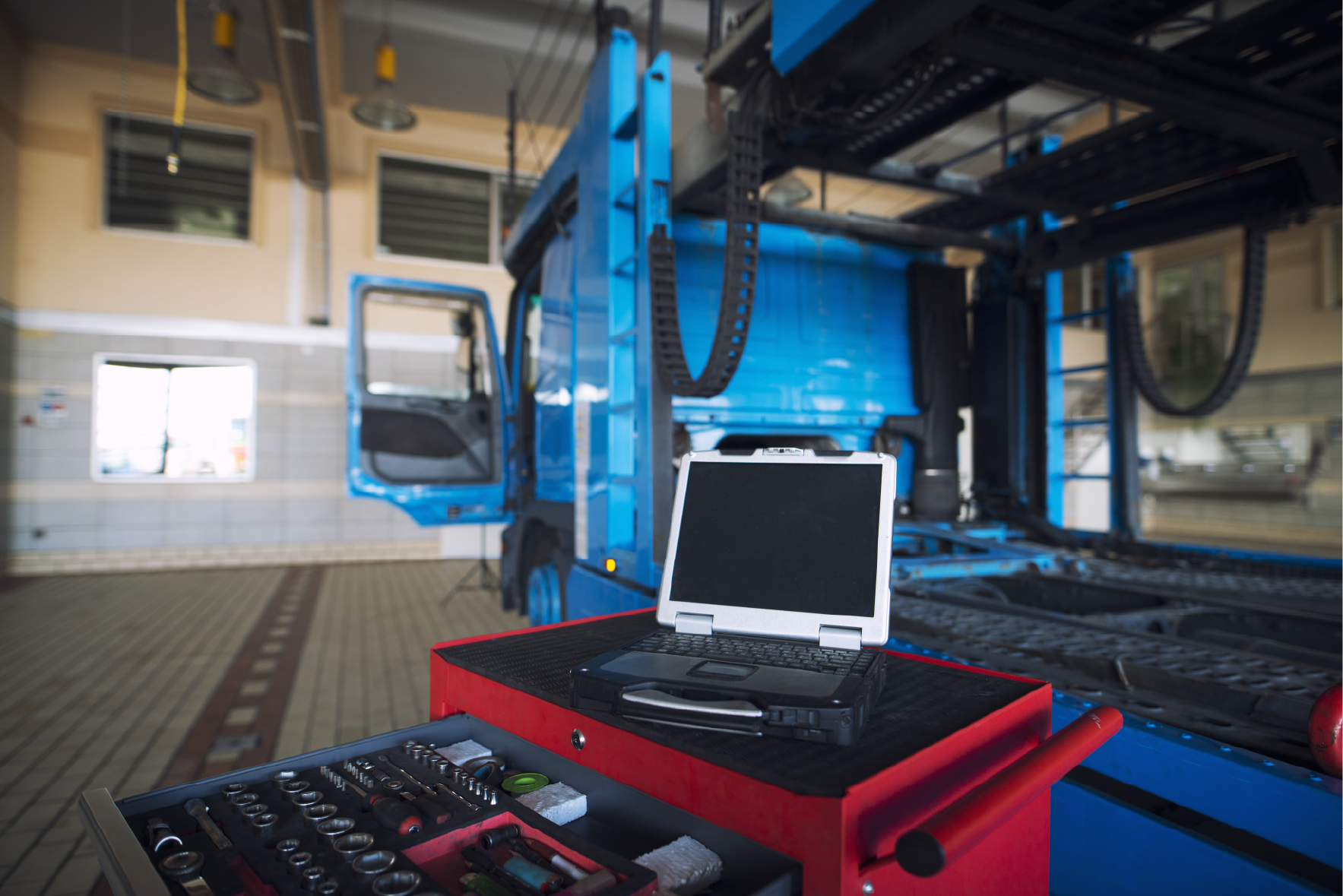 Truck on diagnostic bay in an accredited workshop — rugged laptop and tool chest in foreground, vehicle on lift in background